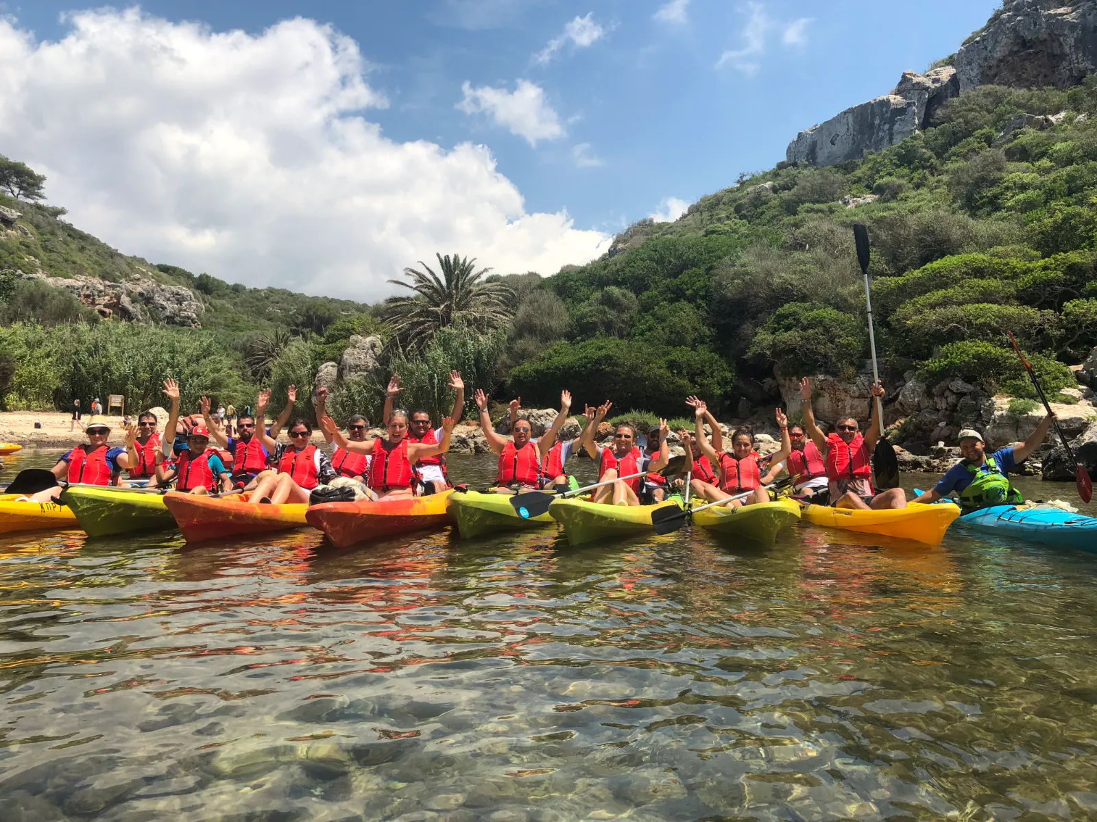 Groupe portant des gilets de sauvetage saluant depuis des kayaks dans une crique de Menorca