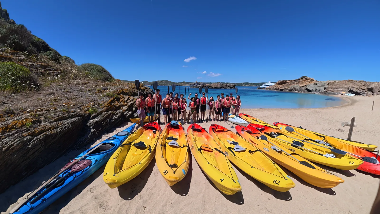 Groupe portant des gilets avec des kayaks alignés sur une plage de Menorca