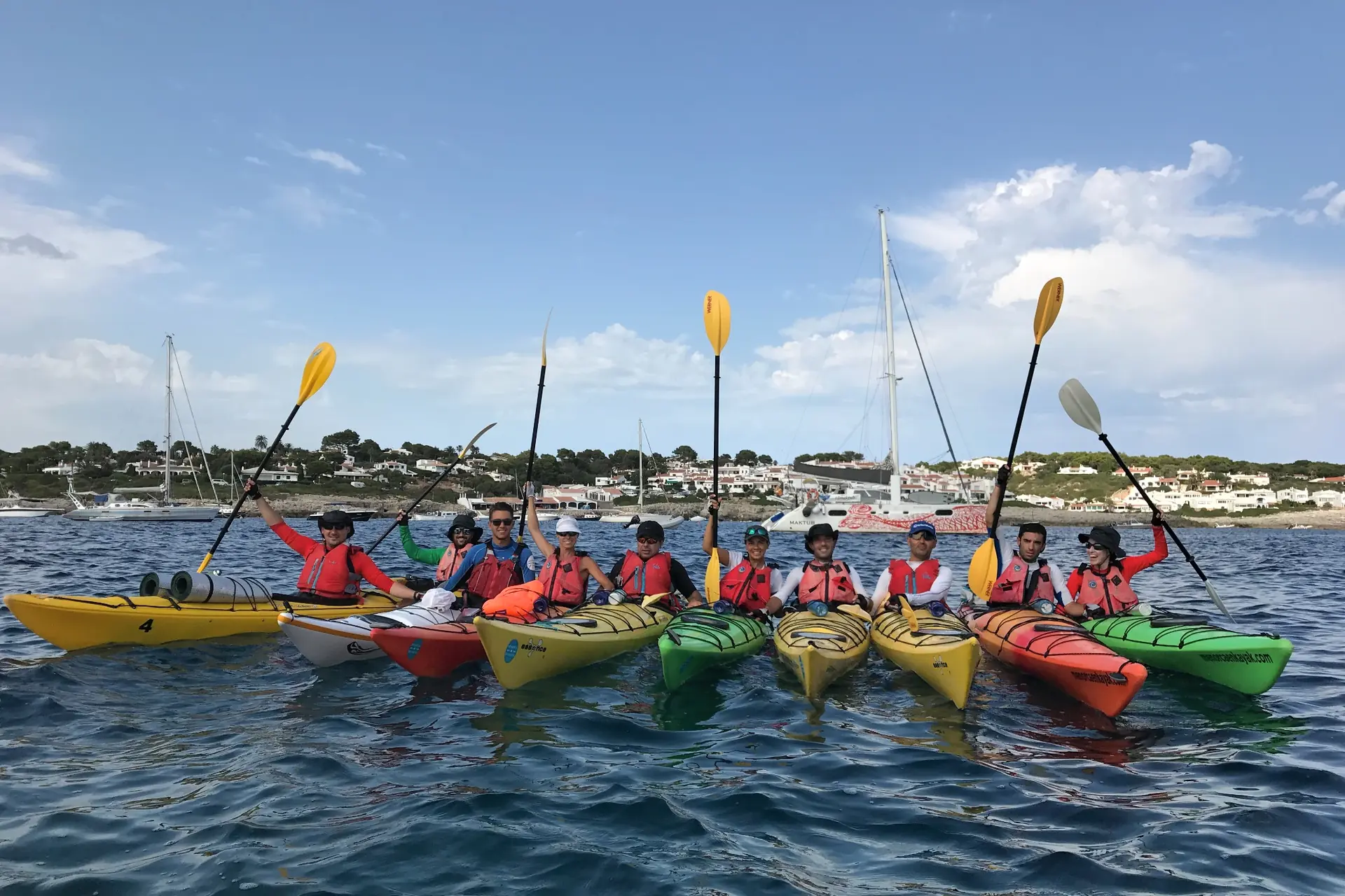 Groupe en kayaks de mer levant les pagaies devant la côte de Menorca